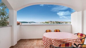A balcony with a table and chairs, a tiled floor, and a view of a distant town across a body of water.