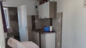 Una habitación pequeña y funcional con cama, kitchenette y baño al fondo.