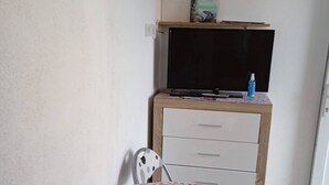 Una habitación pequeña con un escritorio de madera, una silla, un televisor y un aire acondicionado.