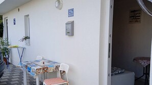 Un pequeño espacio al aire libre con una mesa, sillas, una planta en maceta y una puerta que da a una habitación.