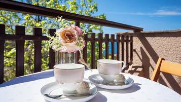 Ein Tisch mit zwei Tassen und Untertassen, einer Blumenvase und einem Cupcake auf einer sonnigen Terrasse.