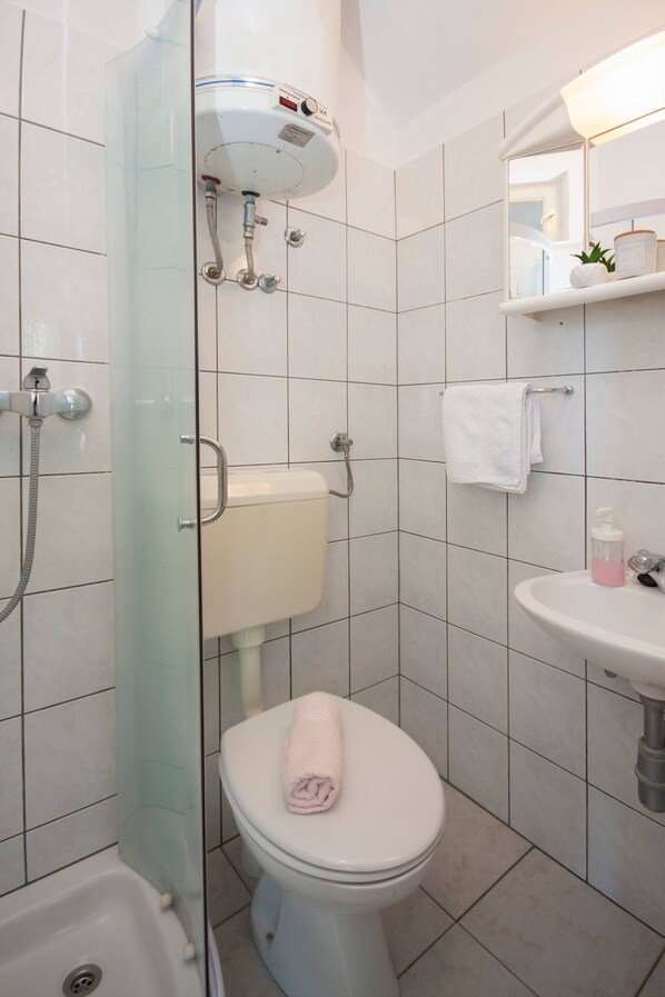 Un baño con cabina de ducha de vidrio, inodoro, lavamanos y espejo.