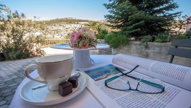 Une table avec une tasse, une soucoupe et des chocolats, un livre ouvert et une paire de lunettes.