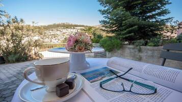 Ein Tisch mit Tasse, Untertasse und Pralinen, ein offenes Buch und eine Brille.