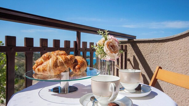 A table with a croissant on a glass stand, two cups, and a small vase with flowers.