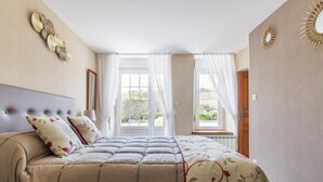 Ein Schlafzimmer mit einem großen Bett, einem Kopfteil, zwei Fenstern mit Vorhängen und einem Wanddekor.