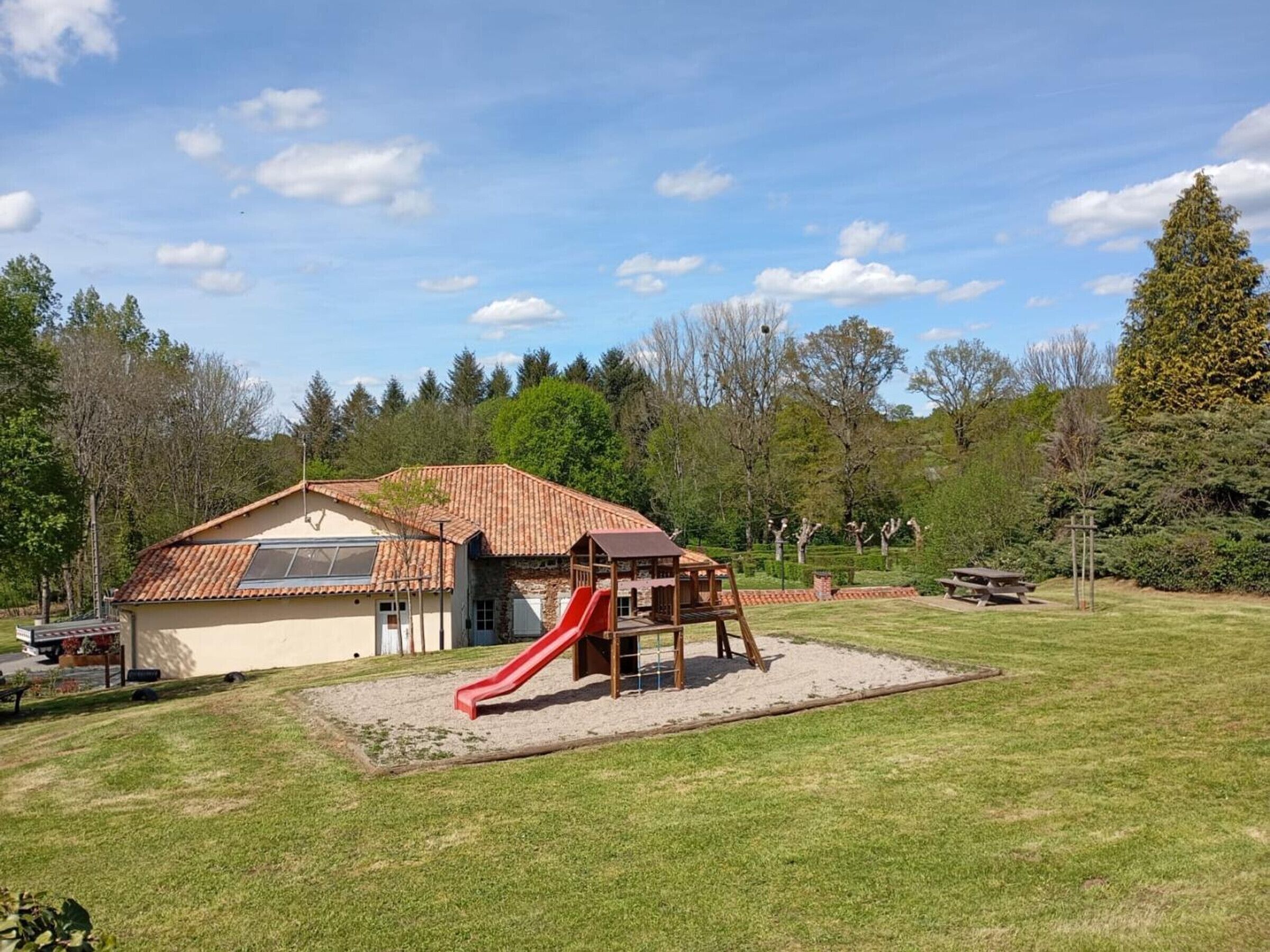 A playground with a slide, a picnic table, and a building with a red roof.