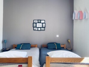 A room with two beds, a wall-mounted picture frame, and a bedside lamp.