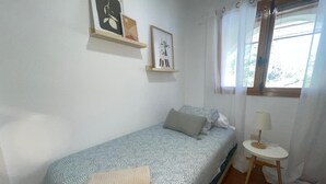 Une petite chambre à coucher, bien rangée, avec un lit simple, une table de chevet avec une lampe et deux tableaux encadrés au mur.