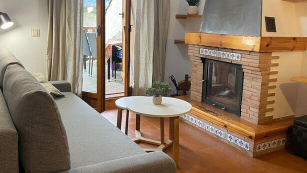 Un salon chaleureux avec une cheminée, un canapé, une petite table avec une plante et une vue sur l’extérieur grâce à une porte coulissante.