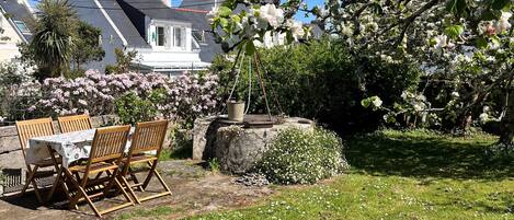 Eine Terrasse mit Tisch und Stühlen, umgeben von blühenden Sträuchern und einem großen Baum mit Blüten.