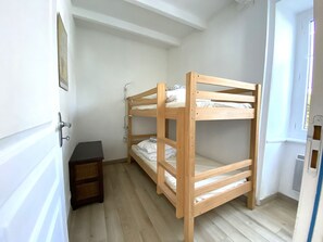 Een slaapkamer met een stapelbed, een klein houten nachtkastje en een deur.