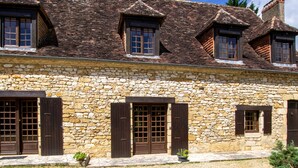 A stone building with multiple windows and doors, featuring a traditional architectural style with a sloped roof.