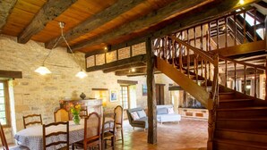 A rustic interior with a dining area, a staircase, and a stone wall.