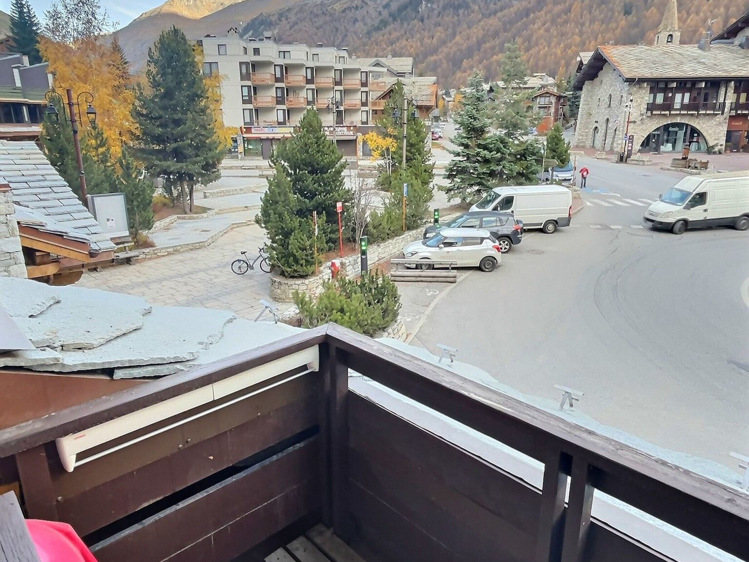 A balcony overlooking a street with parked cars, a bicycle, and buildings with balconies.