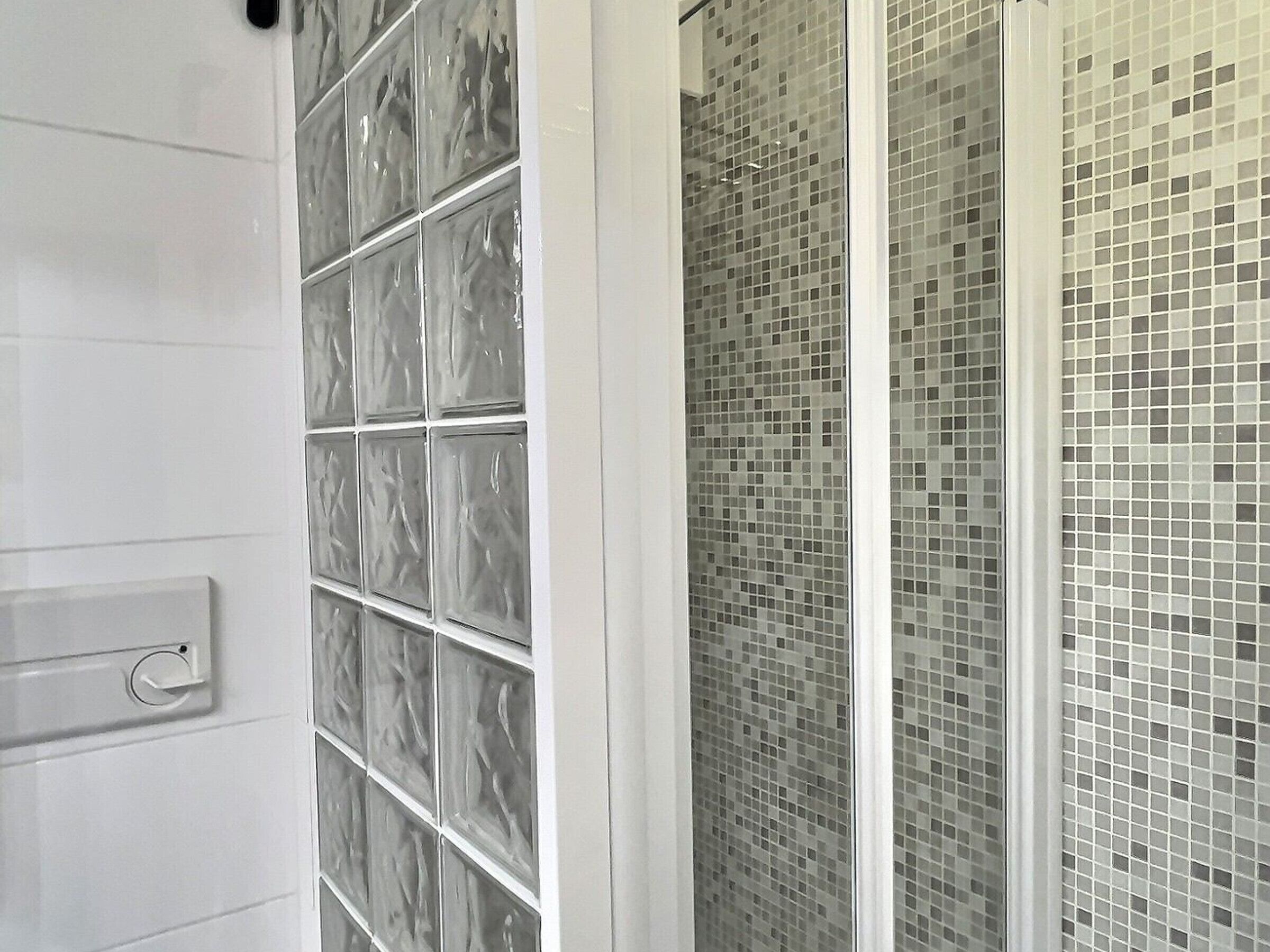 Un baño con pared de azulejos blancos y cabina de ducha de vidrio.