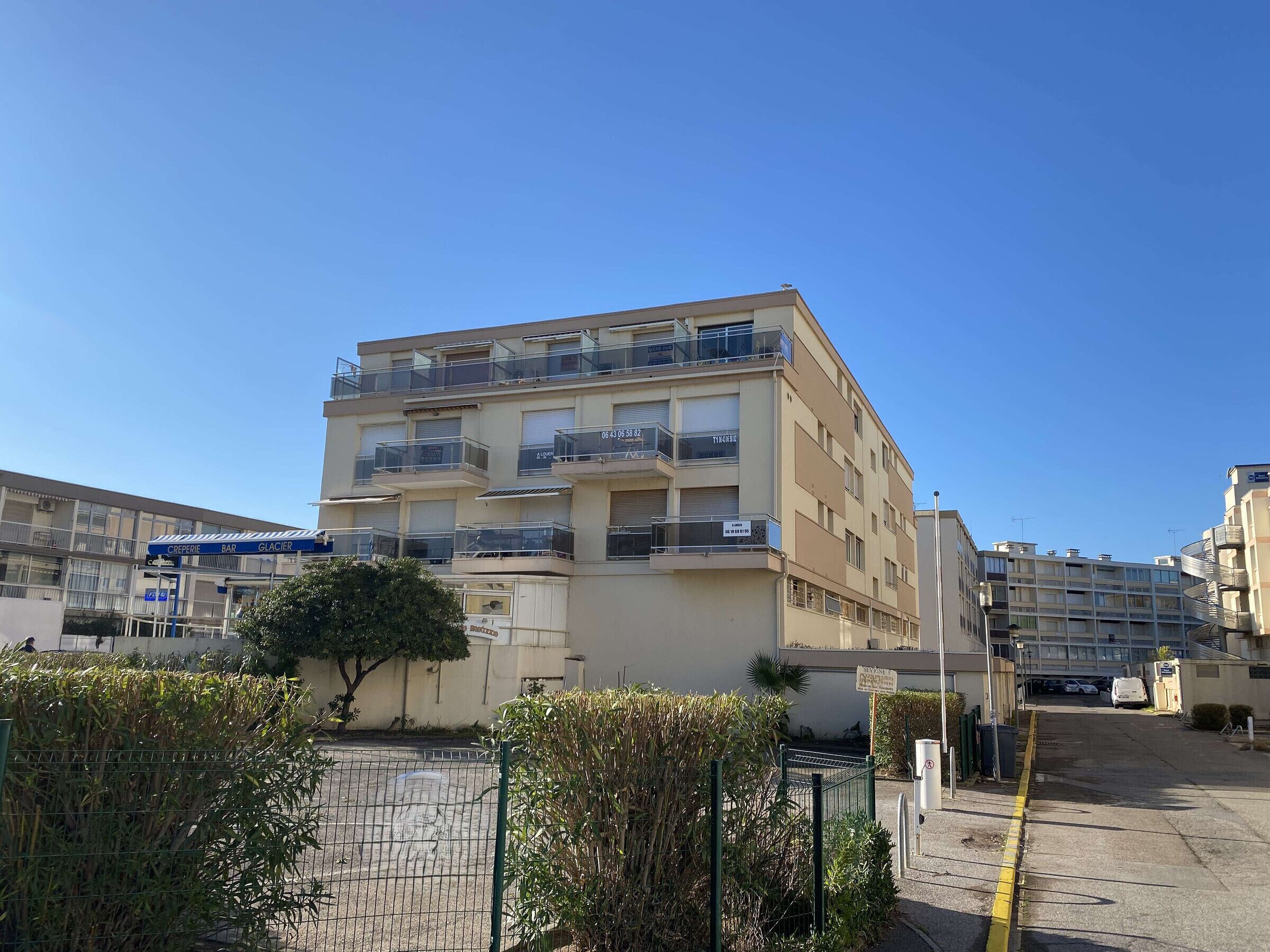 Un immeuble résidentiel à plusieurs étages, doté de balcons, d’un espace de stationnement et surplombant un ciel dégagé.