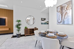A modern dining area with a round table set for six, a wooden console, a large mirror, and artwork on the walls.