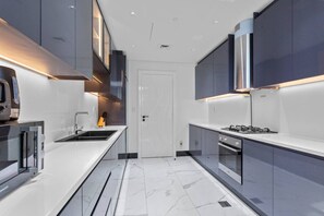A modern kitchen with grey cabinets, a white countertop, a built-in oven, and a stainless steel range hood. - Lush Living w jacuzzi and Burj Khalifa view (Dubai)