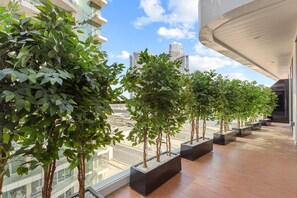 A modern building with a glass facade, a series of potted trees on the balcony, and a view of the cityscape.