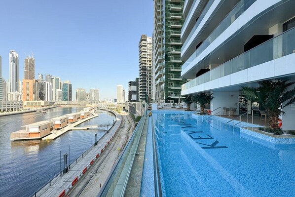Un hotel moderno con piscina en la azotea y vistas a un río, rodeado de edificios altos.