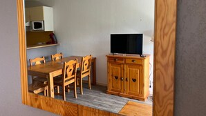 Un coin repas avec une table et des chaises en bois, un téléviseur posé sur un meuble en bois et un four à micro-ondes au-dessus du comptoir.