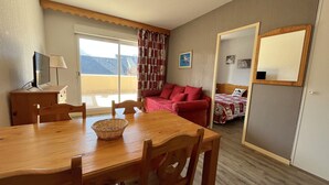A cozy room with a wooden dining table, chairs, a red sofa, a bed with a quilt, and a large window with curtains. - T2 Apartment with terrace and Spassio access, near slopes, 6 people, pet-friendly (Peyragudes)
