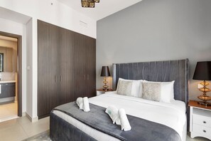 A modern hotel room with a large bed, grey upholstered headboard, and a wardrobe with sliding doors.