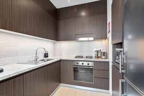 A modern kitchen with dark wood cabinets, a stainless steel sink, and a built-in oven. - Luxury 1 Bedroom in the Heart of Famous Downtown (Dubai)
