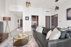 Un salon moderne avec un canapé en cuir, une table basse en verre et un lampadaire. On aperçoit une cuisine à l’arrière-plan, avec un coin repas.