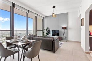 A modern living room with a dining area, large windows, a flat-screen TV, and a floor lamp.