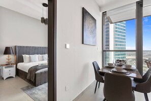 A modern hotel room with a bed, bedside table, lamp, and a dining area with a table set for two. - Luxury 1 Bedroom in the Heart of Famous Downtown (Dubai)