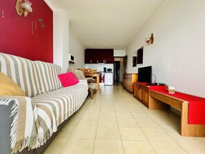Un salon avec un canapé, un téléviseur et une cuisine en arrière-plan.