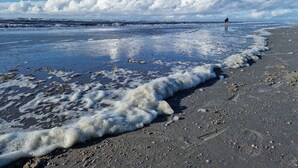 A beach with waves lapping at the shore and a person standing in the distance.