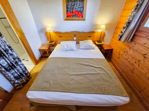 Un dormitorio con cabecera de madera, dos mesitas de noche con lámparas, una cama con ropa blanca y un cuadro enmarcado sobre la cabecera.