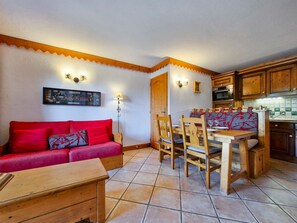 Un espacio de sala acogedor con un sofá rojo, una mesa de comedor de madera y sillas. Hay una cocina con armarios de madera y piso de baldosas.