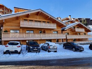 Una cabaña de madera con balcones, un telesilla y un estacionamiento con coches.
