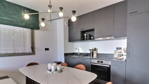 Una cuina moderna amb armaris grisos, un forn de sobre i zona de menjador amb taula i cadires de marbre.