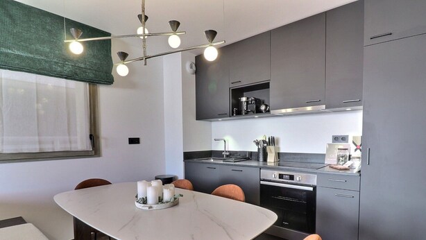 Une cuisine moderne avec des meubles gris, un four encastré et un coin repas comprenant une table et des chaises en marbre.