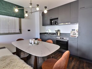 Eine moderne Küche mit grauen Schränken, einem eingebauten Backofen und einem Essbereich mit einem Marmortisch und Stühlen.