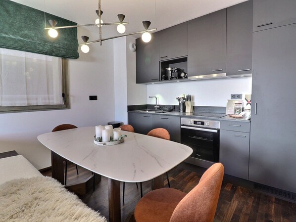 Una cocina moderna con armarios grises, horno empotrado y comedor con mesa y sillas de mármol.