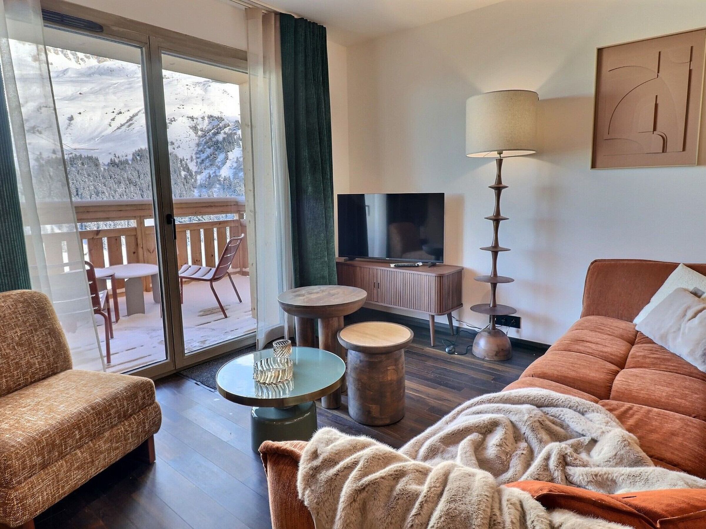Une pièce confortable avec un canapé, un téléviseur, une lampe et une vue sur un paysage enneigé, visible à travers la porte-fenêtre coulissante.