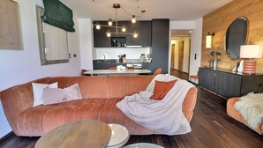 Un saló modern amb un sofà modular, una taula de centre rodona i una zona de menjador amb cuina al fons.
