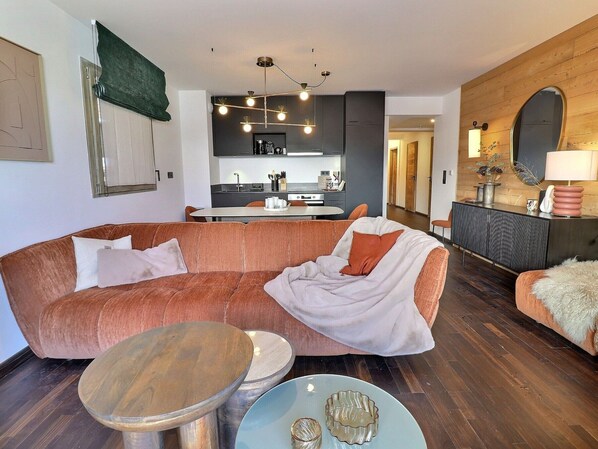 A modern living room with a sectional sofa, a round coffee table, and a dining area with a kitchen in the background.