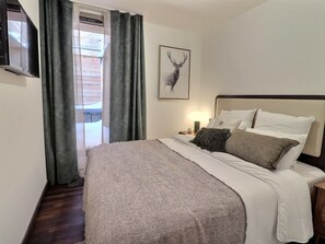 A bedroom with a bed, a nightstand, a lamp, a television, and a deer head artwork.