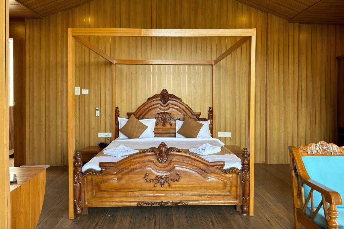 Une pièce aux murs lambrés, avec un grand lit, un bureau en bois et une table entourée de chaises.