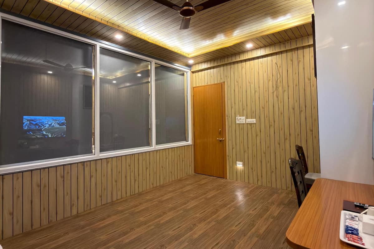 Une pièce aux murs lambrés, dotée d’un ventilateur de plafond, d’un éclairage encastré, d’un plancher en bois et d’une grande fenêtre avec un téléviseur.