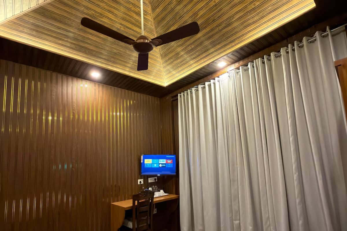 Une chambre d’hôtel équipée d’un lit, d’un bureau avec un ordinateur, d’un ventilateur de plafond et d’une télévision.