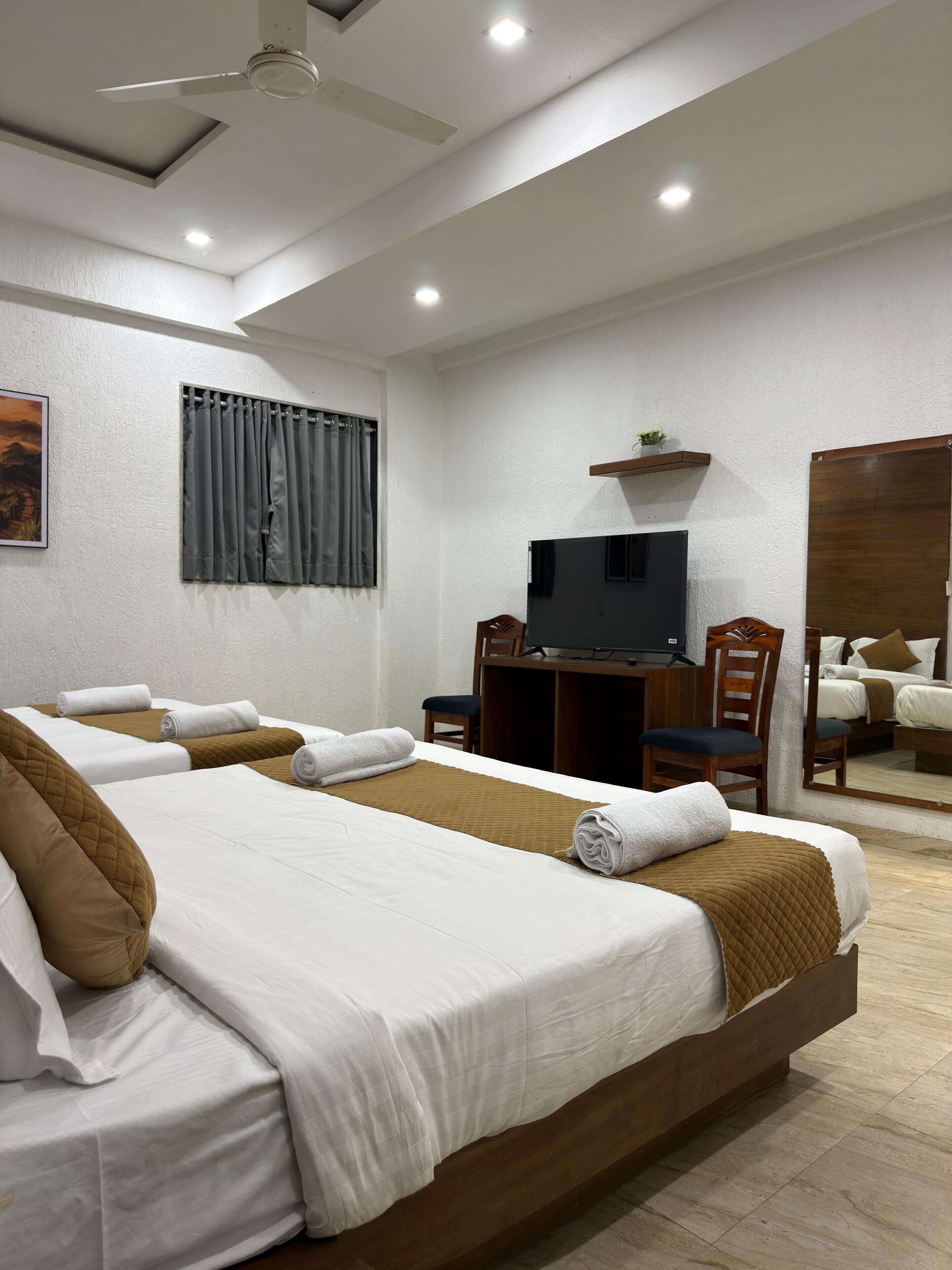 Habitación de hotel con dos camas, un escritorio, un televisor y un espejo.