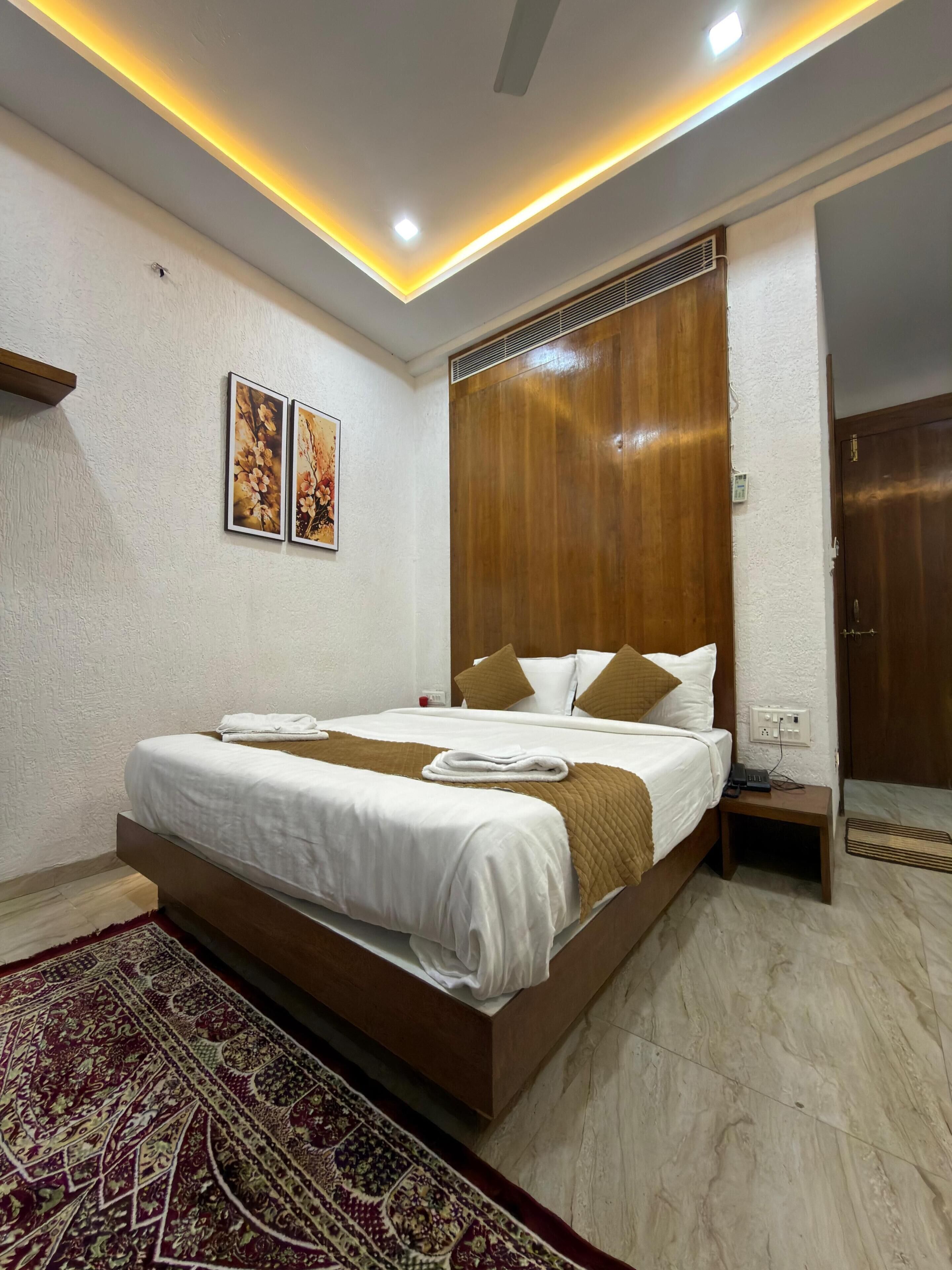 Una habitación de hotel moderna con una cama grande, un cabecero de madera, una mesita de noche pequeña y un aire acondicionado instalado en la pared.